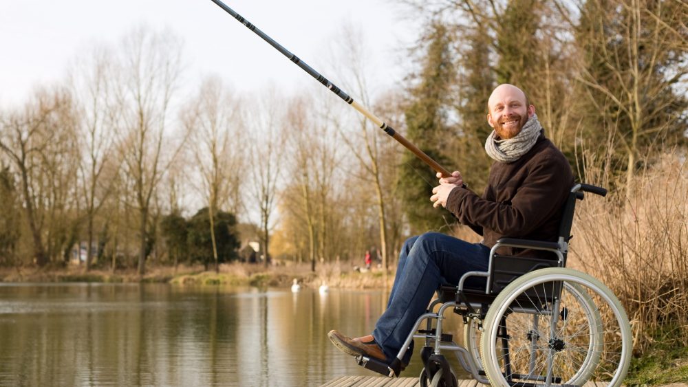 A man in a wheelchair enjoying fishing on the side of a lake