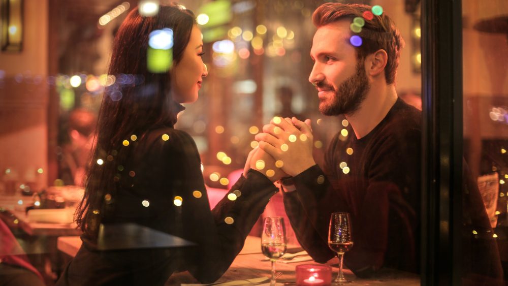 A man and a woman hold hands looking at each other at a restaurant
