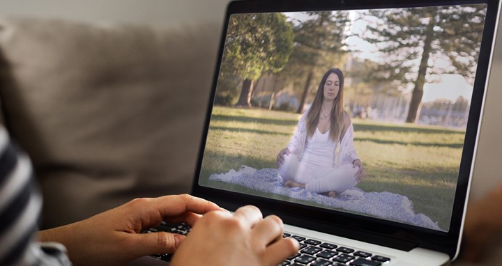 A lady meditating is shown on the laptop screen