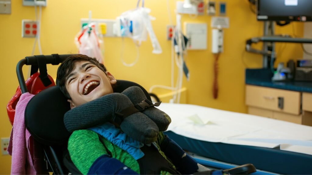 a smiling boy in a wheelchair beside a hospital bed