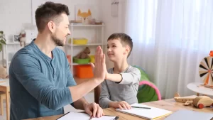 A young boy living with Autism giving his father a high five while they do homework together.