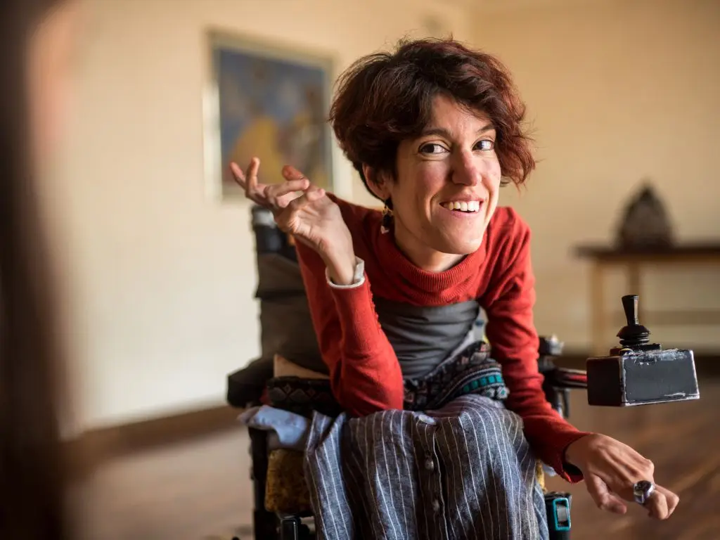 A young woman in her wheelchair, leaning forward and smiling.