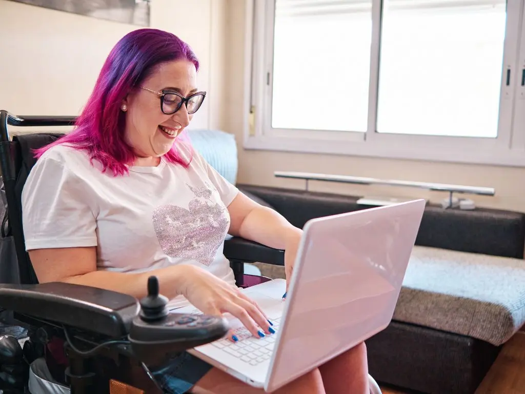 A young woman living with disability browsing on her laptop and smiling.