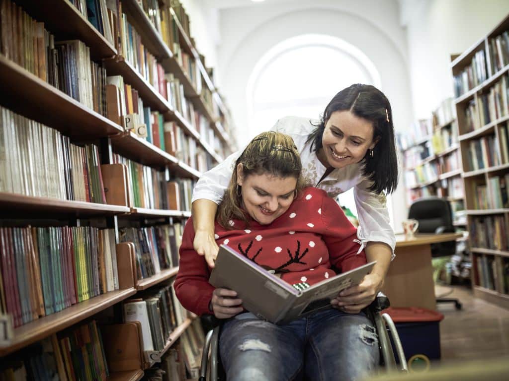 A young woman living with a disability getting support from her carer at the library